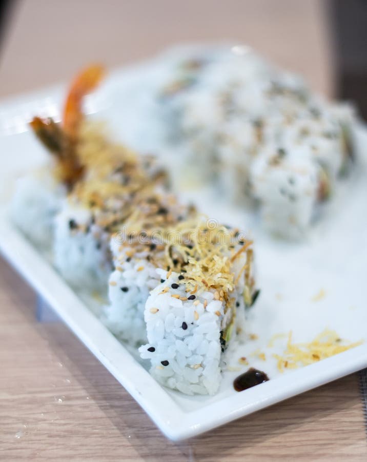 A shoot inside a sushi restaurant with 8 uramaki sushi rolls made from rice, fried scrimp, avocado, philadelphia cheese and seaweed on a white plate. A shoot inside a sushi restaurant with 8 uramaki sushi rolls made from rice, fried scrimp, avocado, philadelphia cheese and seaweed on a white plate.