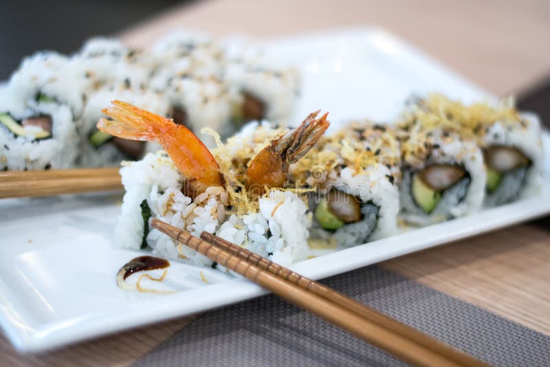 A shoot inside a sushi restaurant with 8 uramaki sushi rolls made from rice, fried scrimp, avocado, philadelphia cheese and seaweed on a white plate. A shoot inside a sushi restaurant with 8 uramaki sushi rolls made from rice, fried scrimp, avocado, philadelphia cheese and seaweed on a white plate.