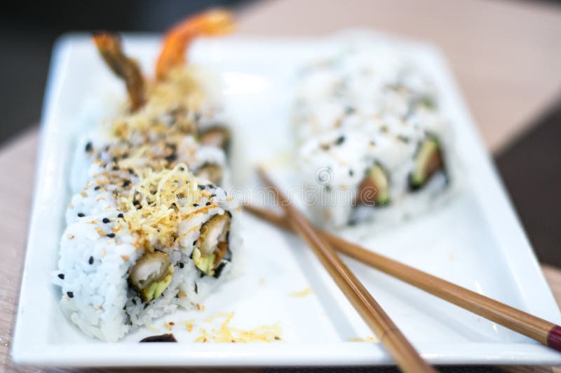 A shoot inside a sushi restaurant with 8 uramaki sushi rolls made from rice, fried scrimp, avocado, philadelphia cheese and seaweed on a white plate. A shoot inside a sushi restaurant with 8 uramaki sushi rolls made from rice, fried scrimp, avocado, philadelphia cheese and seaweed on a white plate.