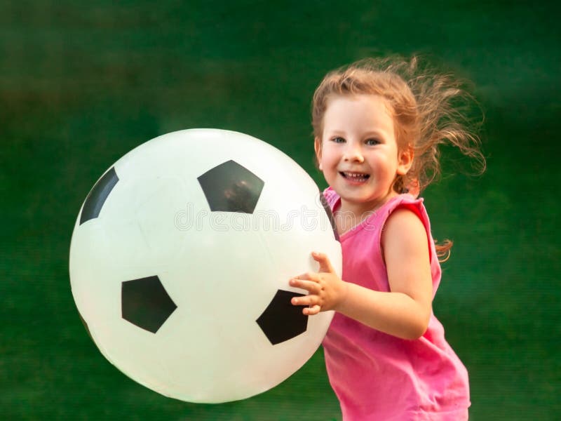 Peu bébé fonctionne avec du ballon de football énorme La fille se réjouit et sourit photos libres de droits Peu bébé fonctionne avec du ballon de football énorme La fille se réjouit et sourit photos libres de droits