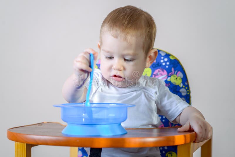 Peu bébé garçon apprenant à manger à une table étudiant un plat et une cuillère dans la cuisine images libres de droits Peu bébé garçon apprenant à manger à une table étudiant un plat et une cuillère dans la cuisine images libres de droits