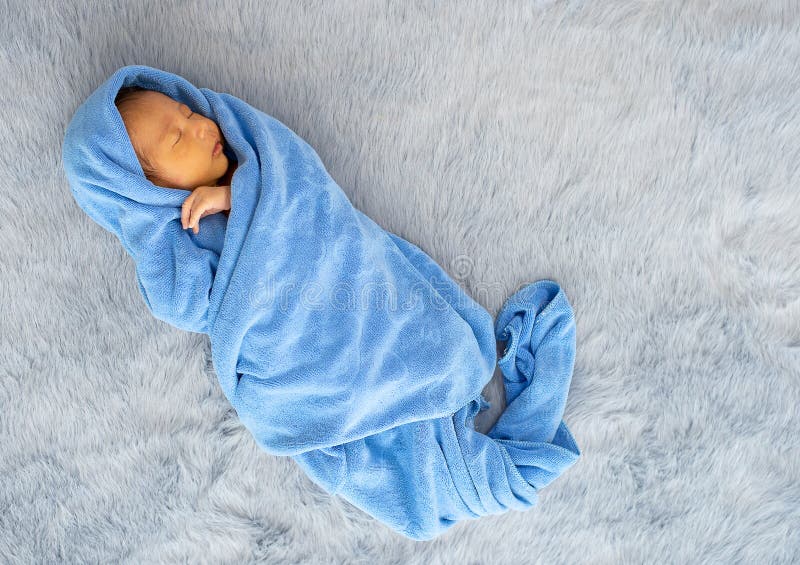 Peu bébé nouveau-né est enveloppé avec la serviette bleue et le bébé dort sur le tapis gris photos libres de droits Peu bébé nouveau-né est enveloppé avec la serviette bleue et le bébé dort sur le tapis gris photos libres de droits