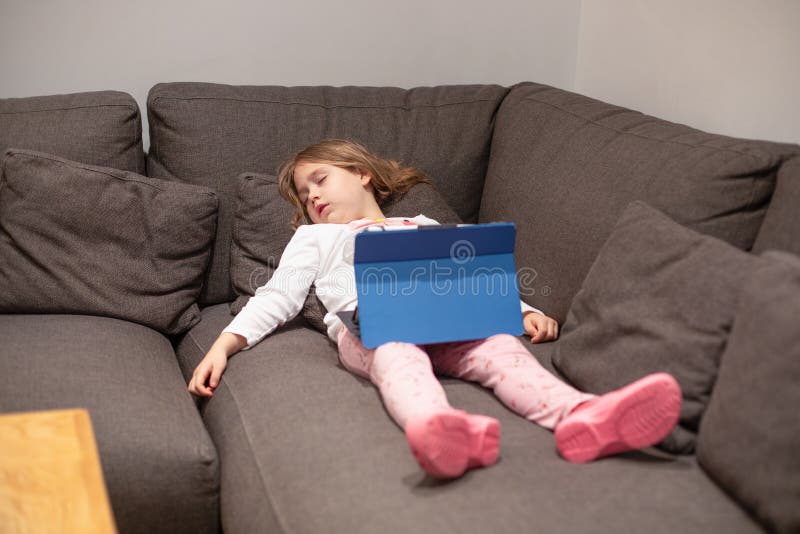Peu de comprimé numérique de observation de sommeil de fille se trouvant sur le couc photos stock