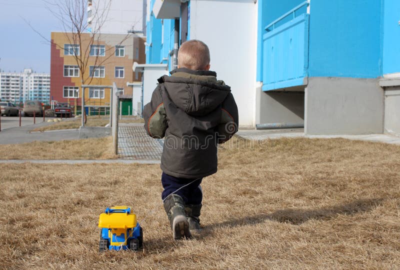Peu de garçon a tourné le sien marchant de retour avec la machine de jouet sur la rue image stock Peu de garçon a tourné le sien marchant de retour avec la machine de jouet sur la rue image stock