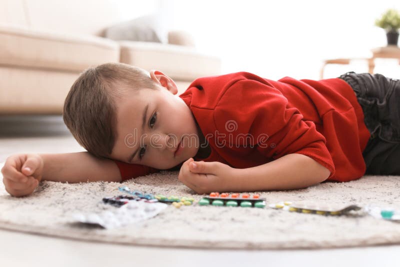 Peu enfant avec des pilules se trouvant sur le plancher Danger de ménage images stock Peu enfant avec des pilules se trouvant sur le plancher Danger de ménage images stock