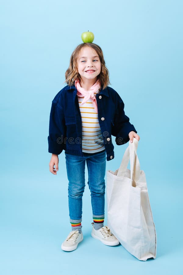 Peu fille avec une pomme sur sa tête tient le sac d'eco photographie stock Peu fille avec une pomme sur sa tête tient le sac d'eco photographie stock