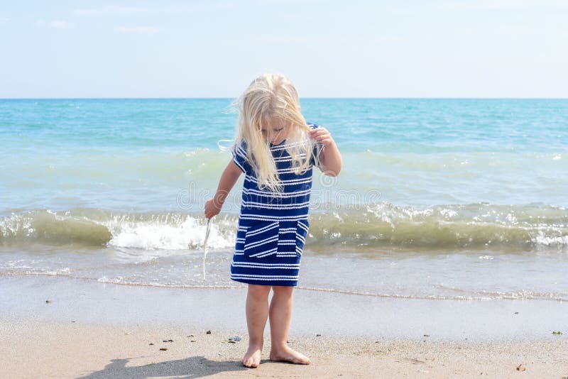 Peu fille blonde marchant sur la plage, tenant une plume photo stock Peu fille blonde marchant sur la plage, tenant une plume photo stock