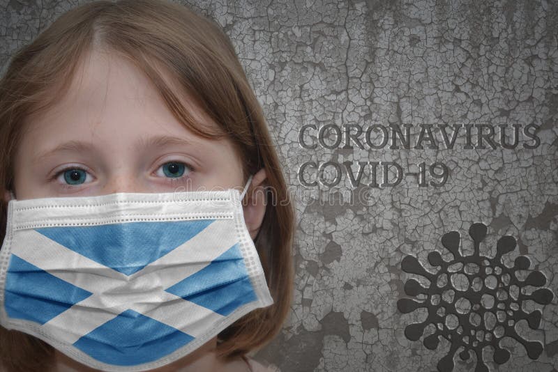 Little girl in medical mask with flag of scotland stands near the old vintage wall with text coronavirus, covid, and virus picture. Stop virus. Little girl in medical mask with flag of scotland stands near the old vintage wall with text coronavirus, covid, and virus picture. Stop virus