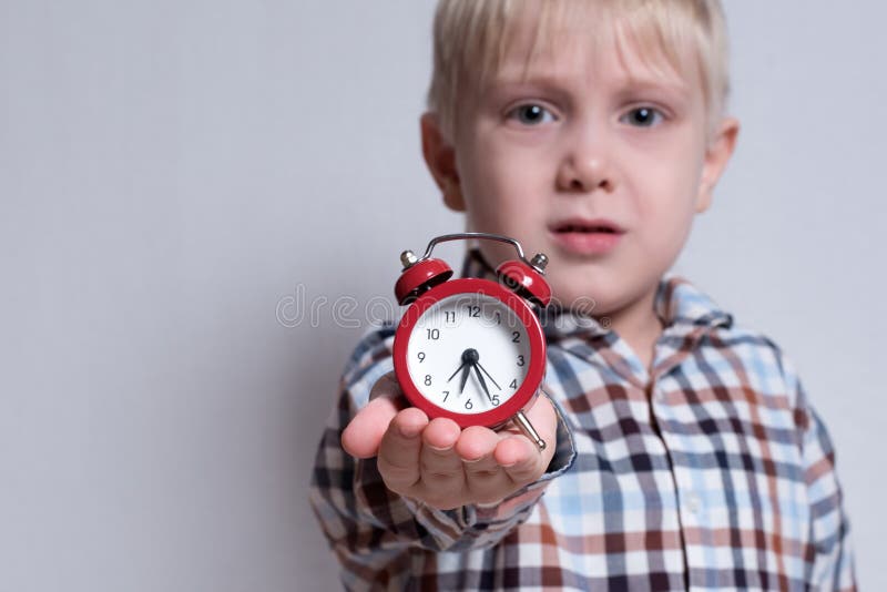 Peu gar? on blond avec un r? veil rouge dans des ses mains Concept de matin Fond clair image stock