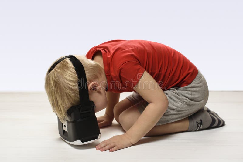 Peu garçon dans une chemise rouge éprouve la réalité virtuelle se reposant sur le plancher Isolat sur le fond blanc Concept de te photographie stock libre de droits