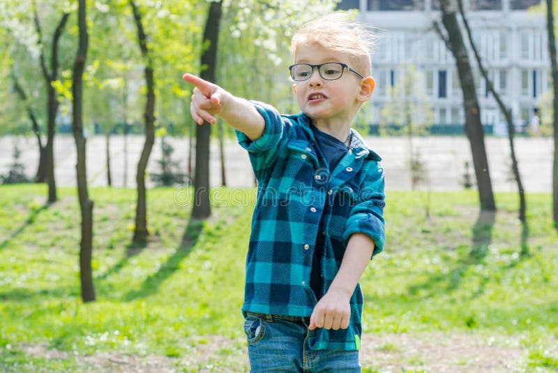 Peu garçon étonné en verres montre quelque part avec un doigt dans le parc image stock
