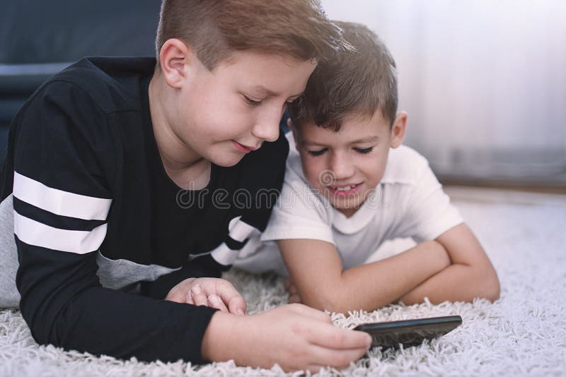 Peu garçons utilisant le smartphone sur le tapis image libre de droits Peu garçons utilisant le smartphone sur le tapis image libre de droits