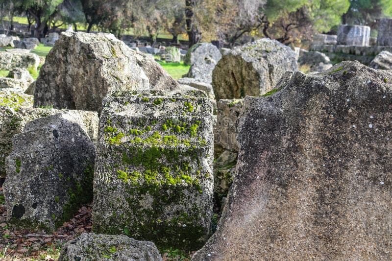 Pezzi caduti di colonne classiche bucate con l'età ed il muschio crescente al sito di Olimpia antico in cui i primi Olympics sono immagini stock libere da diritti Pezzi caduti di colonne classiche bucate con l'età ed il muschio crescente al sito di Olimpia antico in cui i primi Olympics sono immagini stock libere da diritti