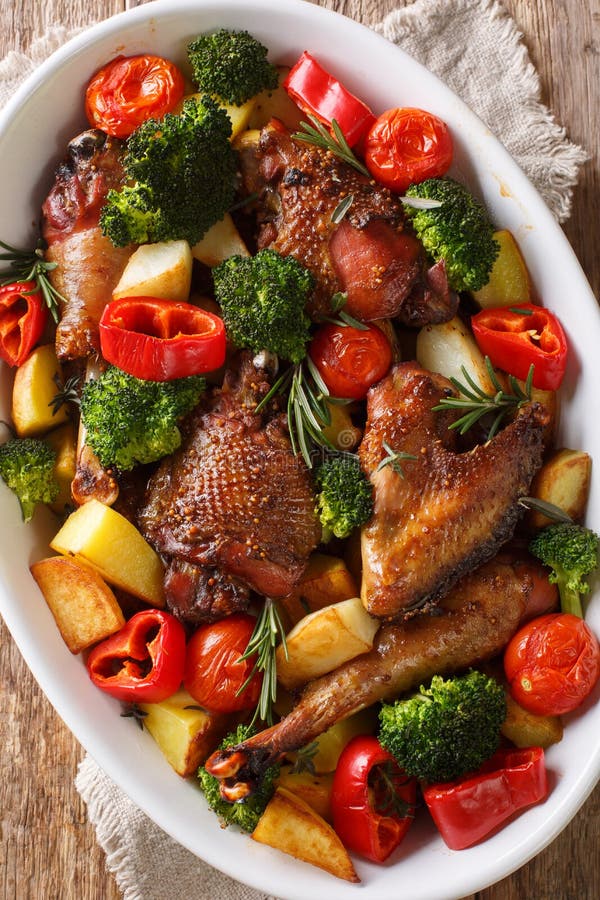 Pezzi di pollo cotti con patate, broccoli, pomodori e pepe chiusi in un piatto da forno Vista dall'alto verticale fotografia stock Pezzi di pollo cotti con patate, broccoli, pomodori e pepe chiusi in un piatto da forno Vista dall'alto verticale fotografia stock