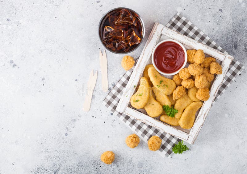 Pezzi di pollo imburrati e morsi di popcorn in una scatola di legno d'annata bianca con ketchup e bicchiere di cola su fondo legg fotografia stock libera da diritti Pezzi di pollo imburrati e morsi di popcorn in una scatola di legno d'annata bianca con ketchup e bicchiere di cola su fondo legg fotografia stock libera da diritti