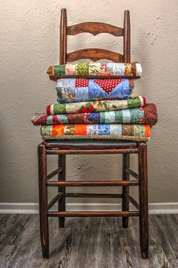 Five colorful handmade quilts folded and displayed on a retro ladder-back dinning table chair. Five colorful handmade quilts folded and displayed on a retro ladder-back dinning table chair.