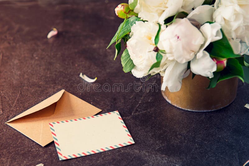 A peônia branca floresce o ramalhete, o cartão vazio e o envelope de papel do ofício no fundo da pedra do preto escuro Vintage qu fotos de stock royalty free A peônia branca floresce o ramalhete, o cartão vazio e o envelope de papel do ofício no fundo da pedra do preto escuro Vintage qu fotos de stock royalty free