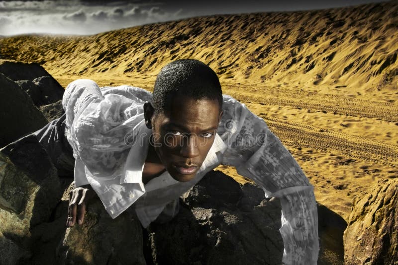 Photo of young man crawling on desert rocks with clouds in background. Photo of young man crawling on desert rocks with clouds in background