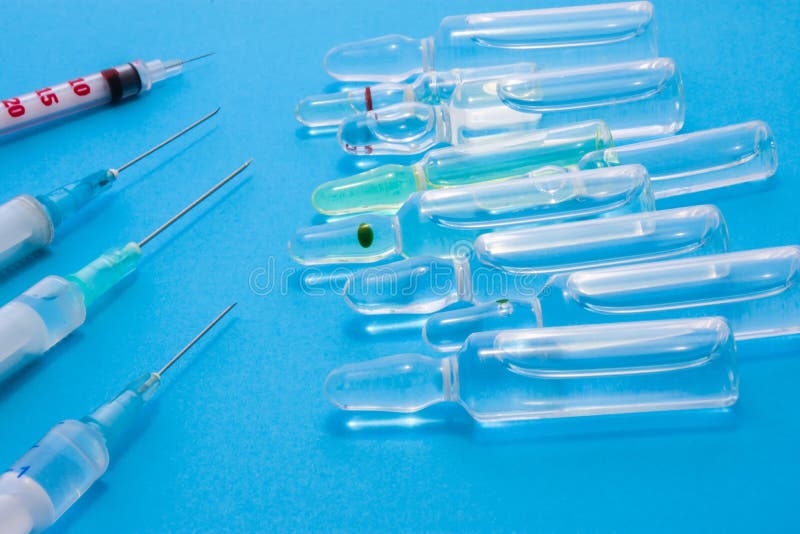 Pharmaceutical glass vials or ampules with liquid drug inside lie near syringes with needles on blue uniform background. Concept p