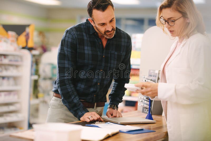 Pharmacien montrant la médecine au client dans la pharmacie image stock Pharmacien montrant la médecine au client dans la pharmacie image stock