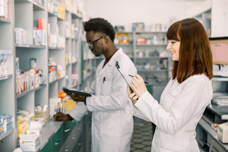 Pharmaciens masculins et f?minins s?rs dans la pharmacie Pharmacien masculin d'afro-américain travaillant au comprimé numérique e photo libre de droits Pharmaciens masculins et f?minins s?rs dans la pharmacie Pharmacien masculin d'afro-américain travaillant au comprimé numérique e photo libre de droits