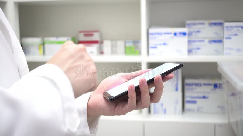 Pharmacist using mobile phone at drugstore room. Doctor touching a cell phone in medical concept