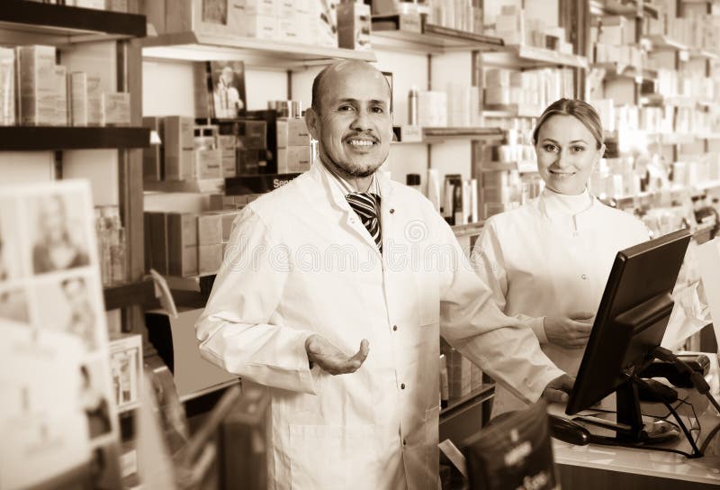 Cheerful smiling pharmacists standing with a cash desk in the pharmacy