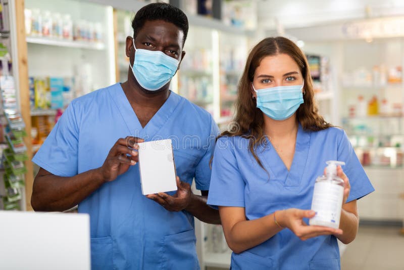 Pharmacists in masks and surgical scrubs standing in salesroom of drugstore. Pharmacists in masks and surgical scrubs standing in salesroom of drugstore
