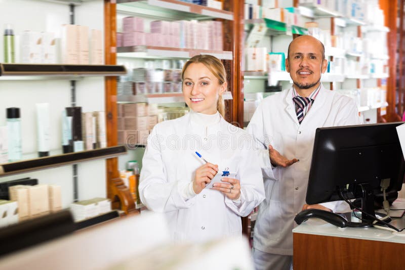 Pharmacists wearing white coats standing next to shelves with medicine. Pharmacists wearing white coats standing next to shelves with medicine