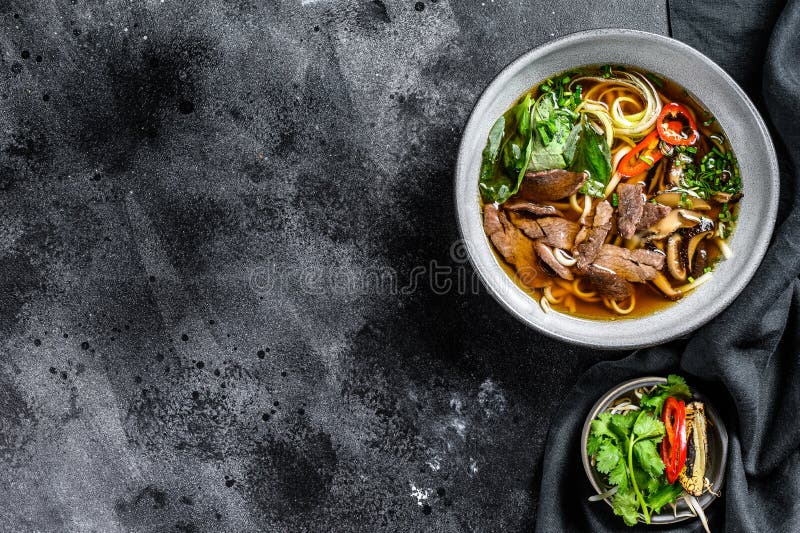 Pho Bo Vietnamese fresh rice noodle soup with beef, herbs and chili. Black background. Top view. Copy space