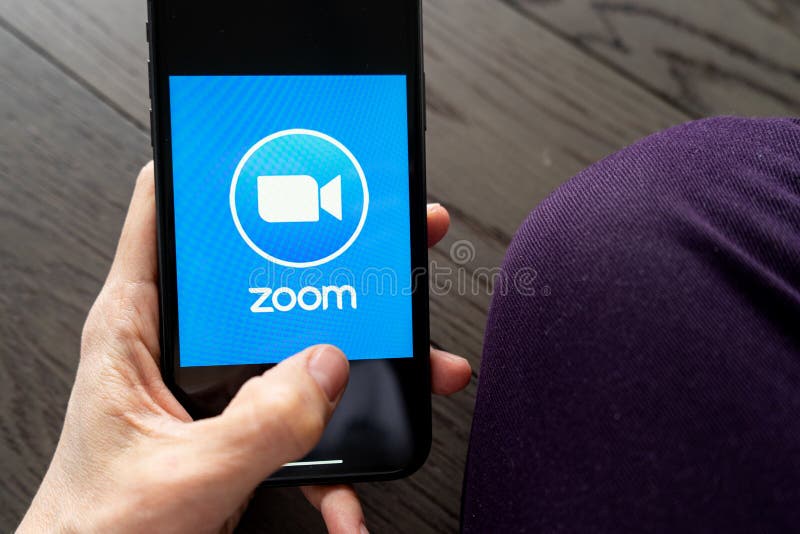 Phone with a hand showing Zoom Cloud Meetings app.