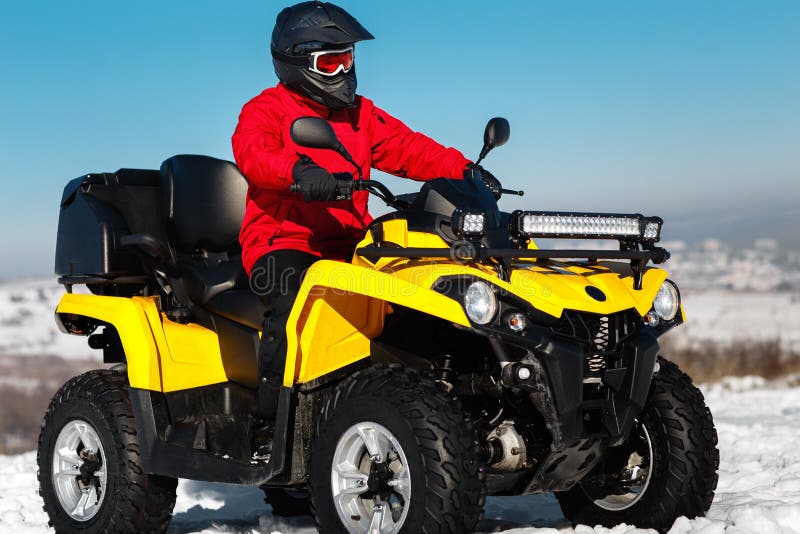 Photo of attractive young man in red warm winter clothes and black helmet on the ATV 4wd quad bike stand in heavy snow