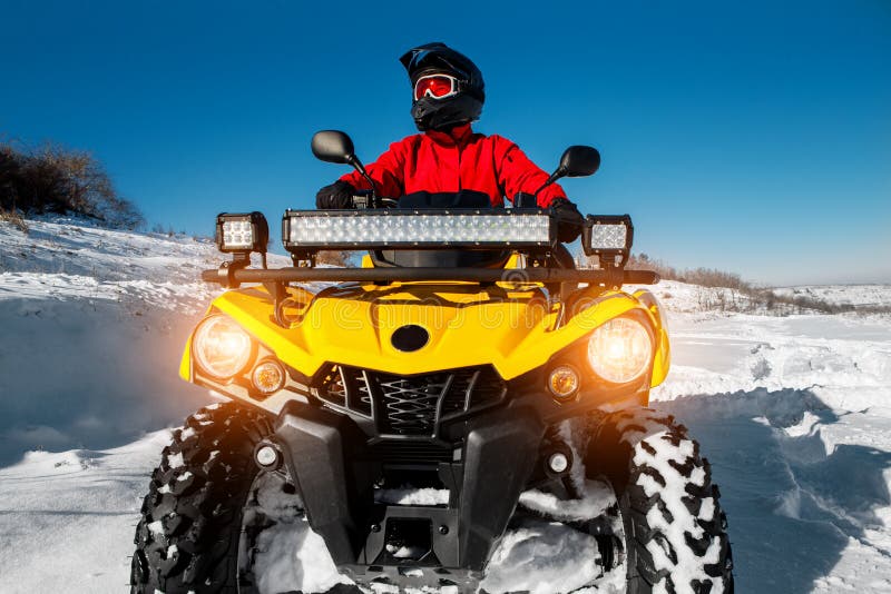 Photo of attractive young man in red warm winter clothes and black helmet on the ATV 4wd quad bike stand in heavy snow