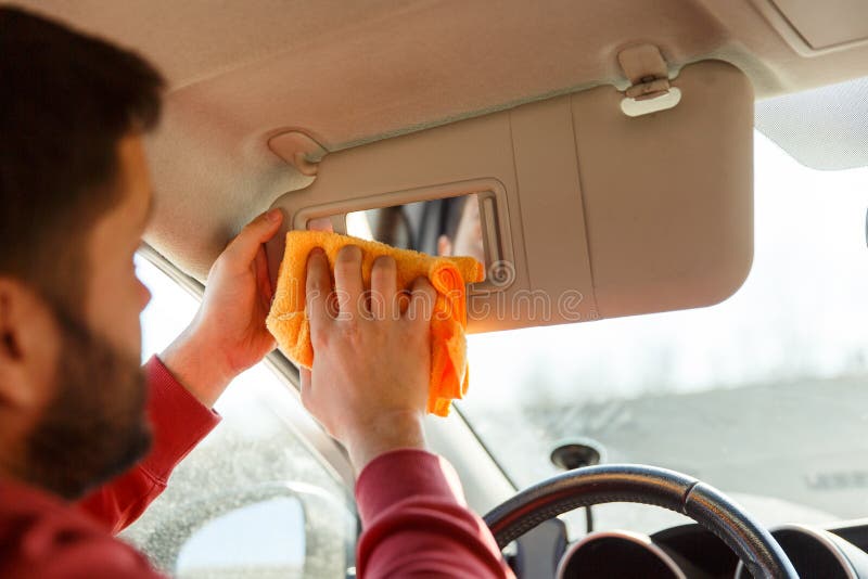 Photo from back of brunet with orange rag washing mirror of car,close up