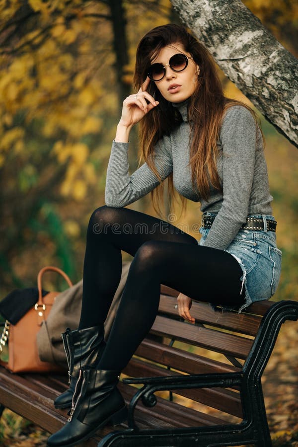 Photo of brunette in sunglasses sitting on bench in autumn park