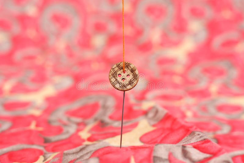 Photo of button and needle in the attached thread stock photo