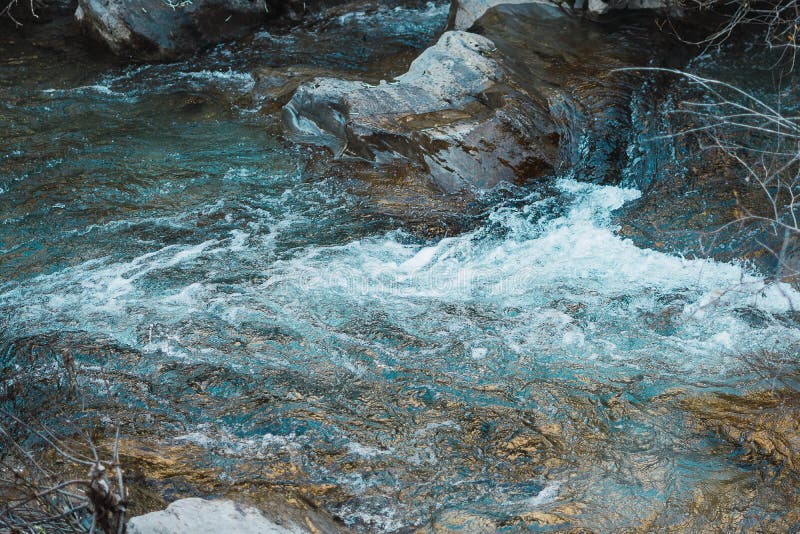 In this photo we can appreciate a blue river with a fast watercourse. the forest is wet and the plants and vegetation are falling over because is autumn. there are some rocks and wooden branches in the water and near the rocks. In this photo we can appreciate a blue river with a fast watercourse. the forest is wet and the plants and vegetation are falling over because is autumn. there are some rocks and wooden branches in the water and near the rocks