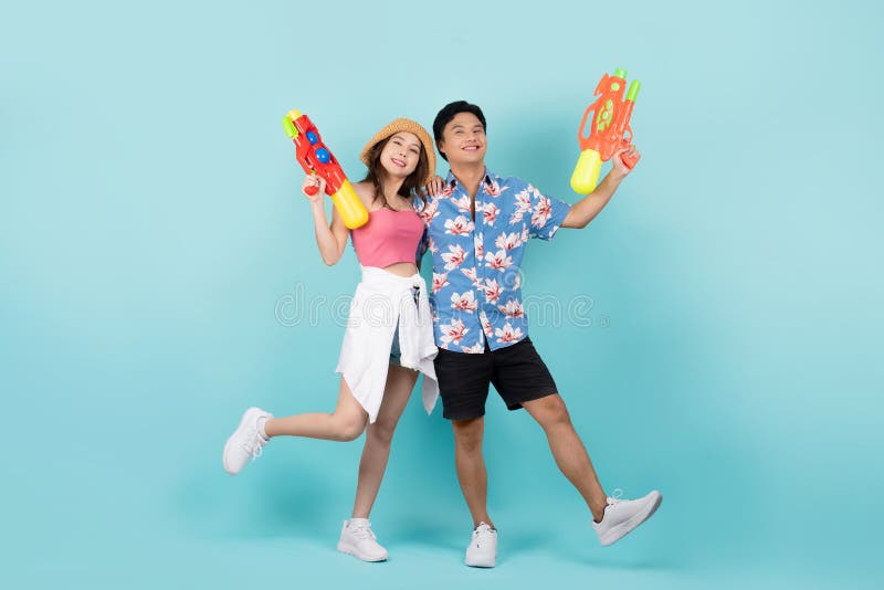 Photo complète du jeune couple asiatique heureux en tenue d'été avec pistolet à eau et regarder la caméra en fond bleu photos libres de droits