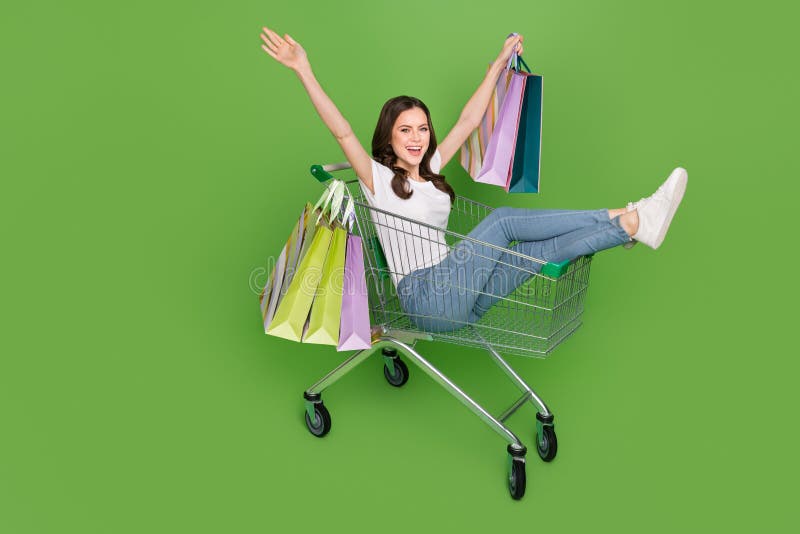 Photo of cute excited young lady wear white t-shirt driving tray rising shopping bags isolated green color background