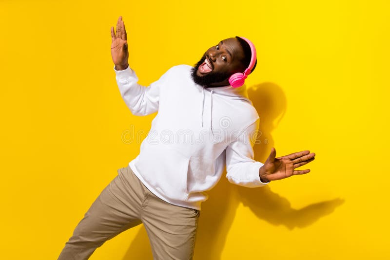 Photo of cute young brunet man dance listen music wear headphones hoodie trousers isolated on yellow background