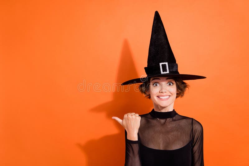 Photo of cute young lady excited impressed point empty space dressed trendy black halloween witch outfit isolated on orange background. Photo of cute young lady excited impressed point empty space dressed trendy black halloween witch outfit isolated on orange background.