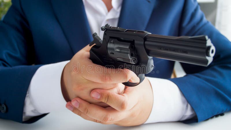 Photo de plan rapproché d'homme d'affaires dans le costume se reposant dans le bureau et tenant le revolver photo libre de droits Photo de plan rapproché d'homme d'affaires dans le costume se reposant dans le bureau et tenant le revolver photo libre de droits