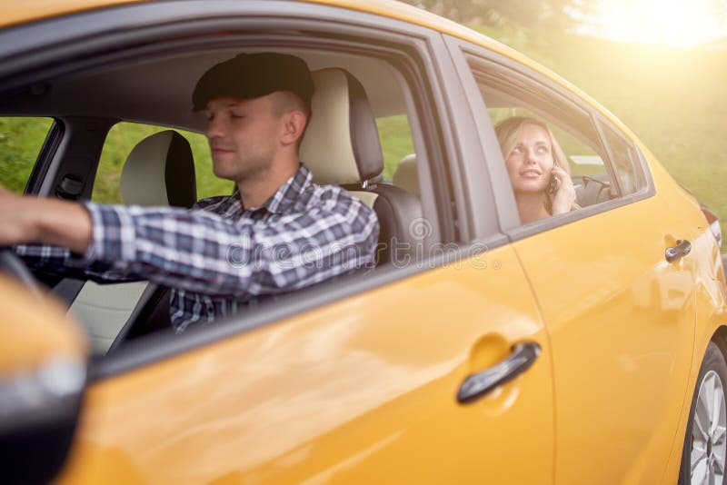 Photo Of Driver Of Yellow Taxi Sitting At Wheel And Blonde Sitting In Back Seat Stock Image