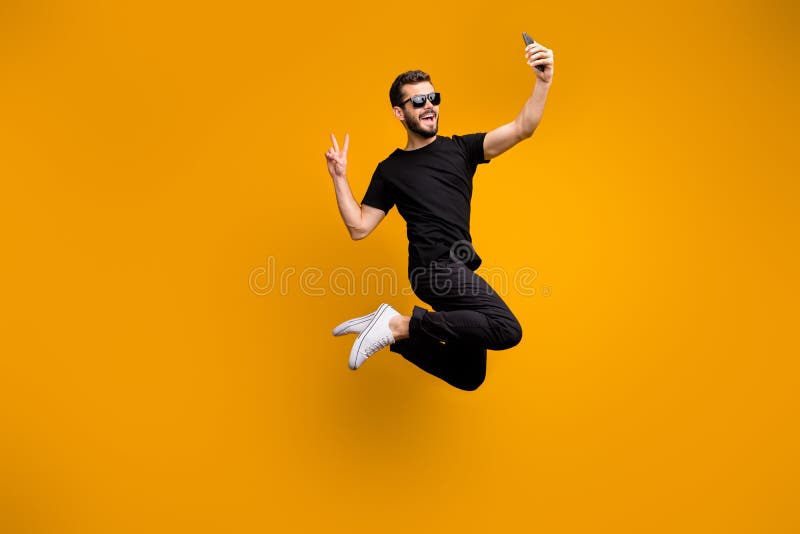 Photo du corps complet d'un hipster fou sautant le haut du téléphone en tenant des selfies montrant un symbole de signe v portant