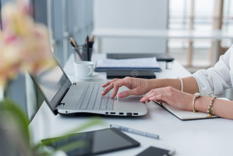 Photo en gros plan des mains femelles avec des accessoires travaillant sur l'ordinateur portable dans un bureau moderne, utilisan photo libre de droits Photo en gros plan des mains femelles avec des accessoires travaillant sur l'ordinateur portable dans un bureau moderne, utilisan photo libre de droits