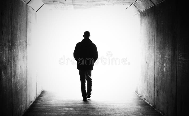 Photo en noir et blanc des mains d'un homme dans les poches de marche à pied dans un tunnel sombre vers la lumière.