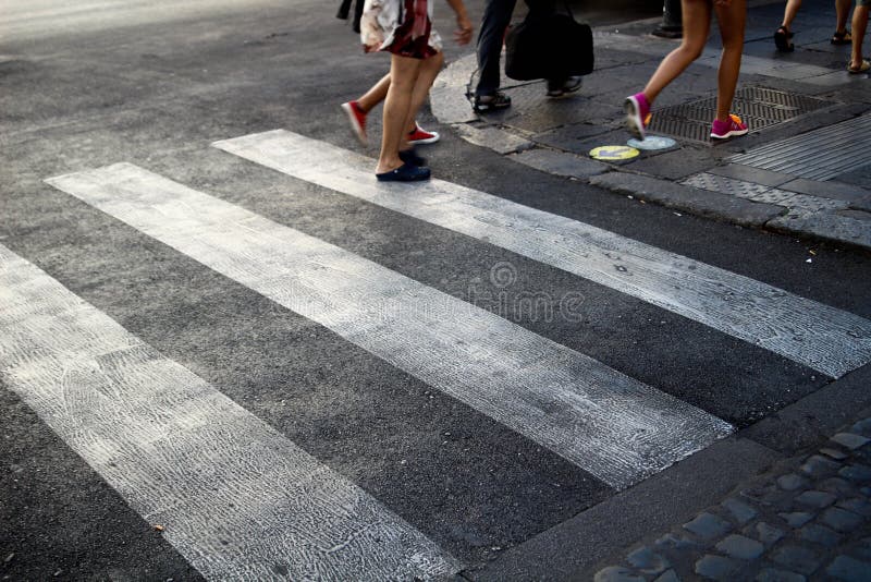 3 people crossing a white Zebra Crossing, on a grey tarmac road, in Central Rome Italy