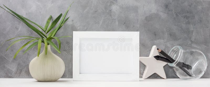 Photo frame close up mock up with palm leaves in vase, ceramic star, pen and pencil in mason jar on shelf. Scandinavian style royalty free stock photography