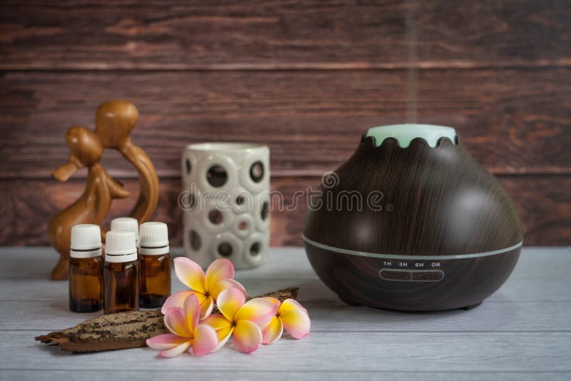 Brown essential oil diffuser with frangipani flowers, candle and small wooden love statue stock image Brown essential oil diffuser with frangipani flowers, candle and small wooden love statue stock image