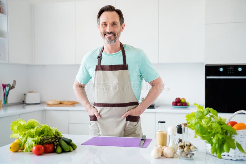 Photo Of Handsome Mature Bearded Man Hands Pockets Wear Kitchenware Apron In Kitchen Apartment 